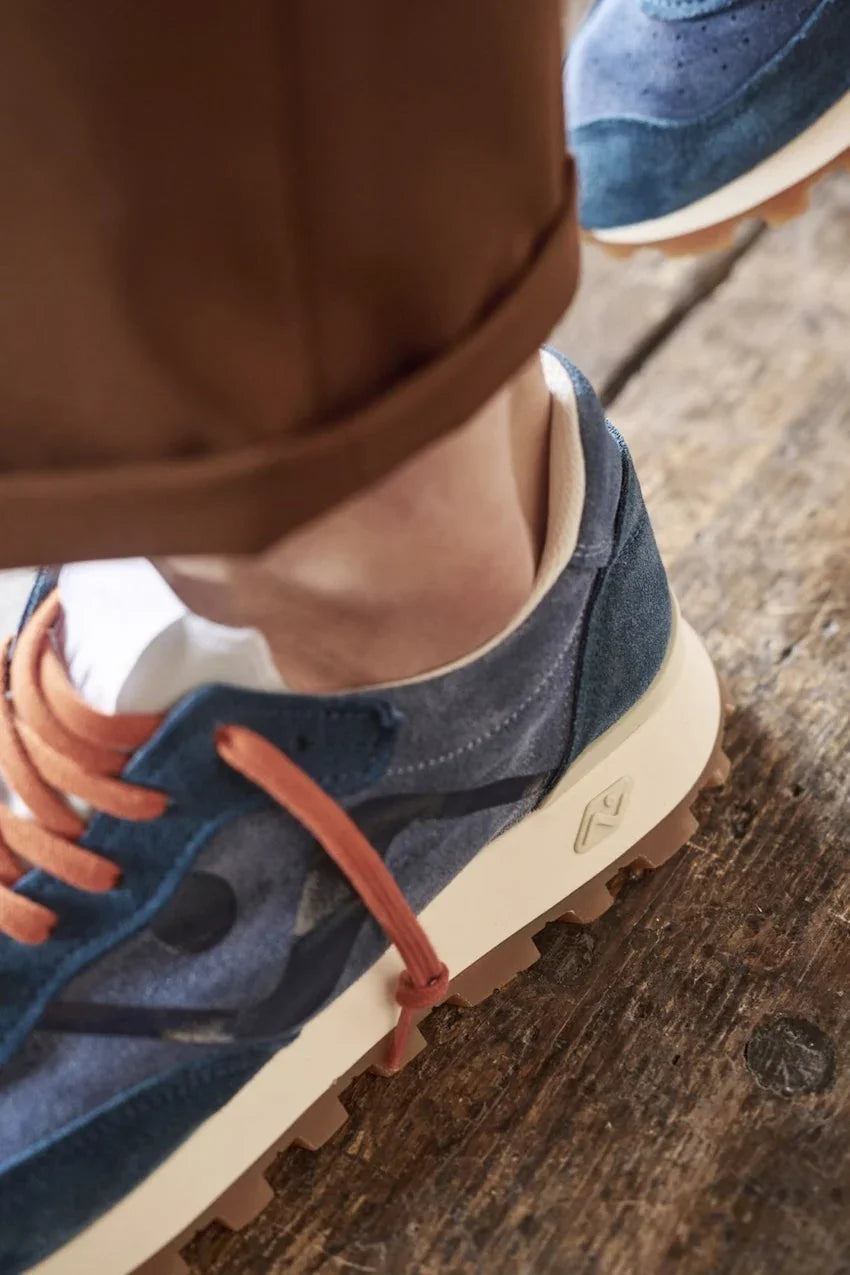 Detailopname van blauwe suède sneakers met bruine veters op een houten vloer.