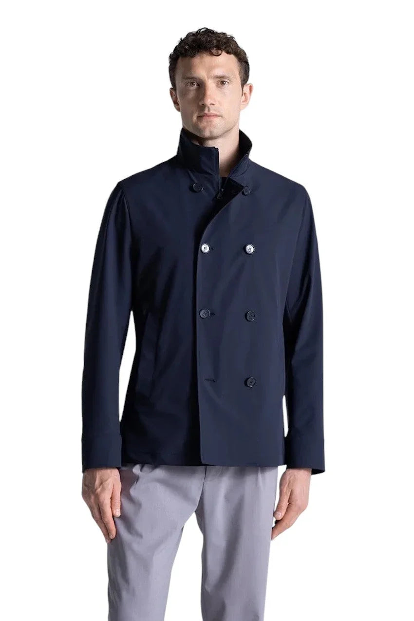 Man in een donkerblauwe dubbelrijige jas met hoge kraag en grijze pantalon.